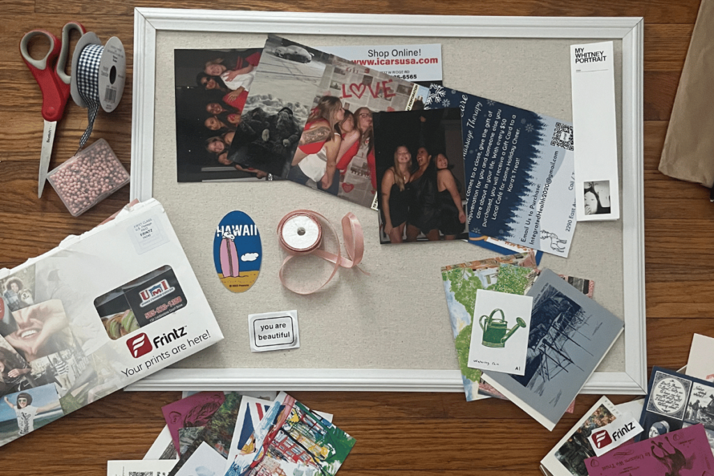 A corkboard layed out on the floor with photo prints, ribbon, a Frintz packet of free photo prints, fun stickers and other college dorm memories.