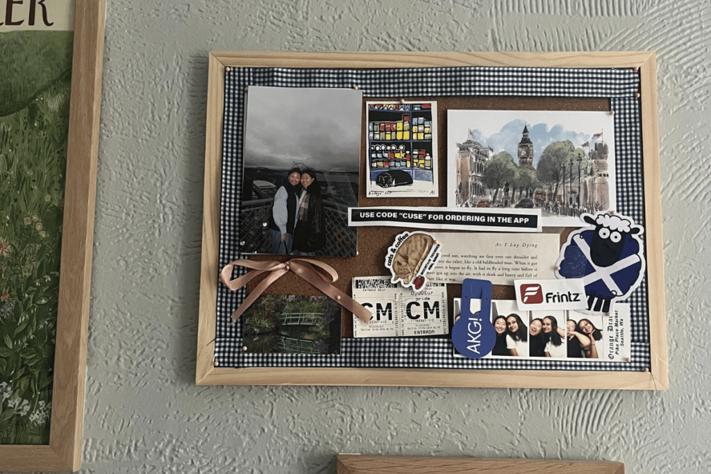 The finalized cork board of college memorabilia and free photo prints hanging up on the wall in a dorm room.