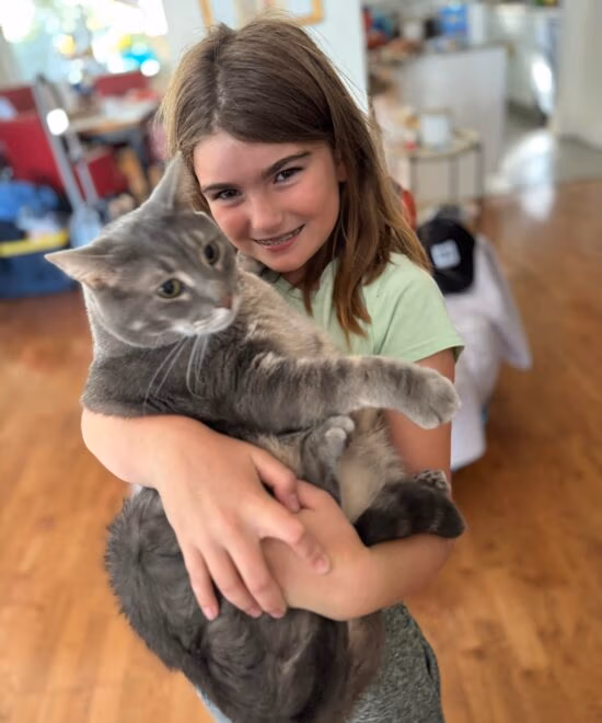 A young girl holds a cat, the girl looks thrilled, the cat looks like he's tolerating her.